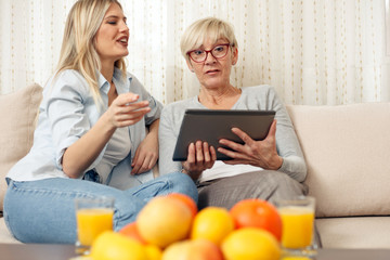 Senior mother and daughter browsing the internet on a tablet. Happy family moments at home.