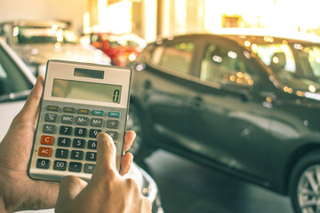 Asian man pressing calculator for business finance on car showroom blurry background.