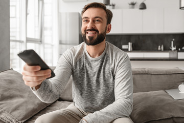 Portrait of a cheerful young man holding TV remote control