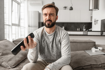 Portrait of a disappointed young man holding TV remote control