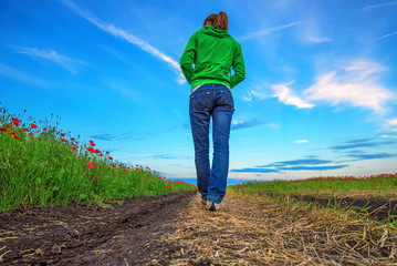 Girl walks on road surrounded with poppy fields