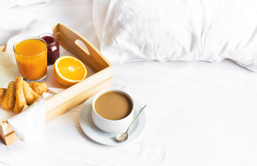 Morning breakfast in bed wooden tray with a cup of coffee croissant orange juice fresh orange jam Bed linen. Top view Hotel Room Early Morning at Hotel Background Concept Interior Copy Space