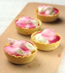 four cakes with cheese cream and red topping on the board