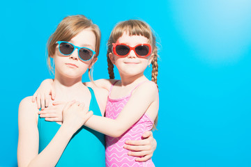 Fototapeta na wymiar Cute girls in swimwear with glasses hugging on blue background