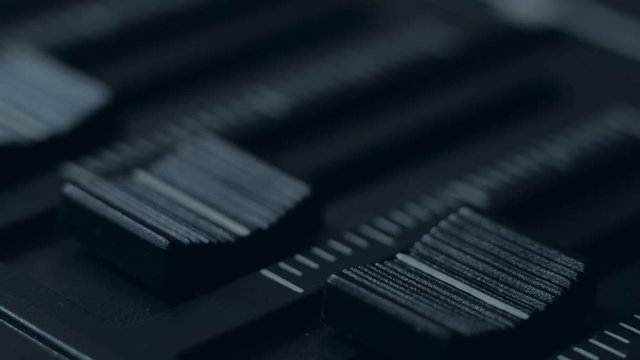 Extreme close up - focused fingers pushing a fader of a mixing console. Professional sound engineer balancing volume of audio inputs of digital audio mixer. Macro footage.