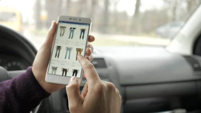 A man looks at the goods in the online clothing store, sitting in the car. Smart phone online shopping.