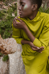 tender african american woman with closed eyes and glitter makeup posing in yellow dress