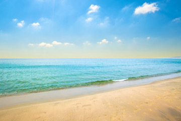 Sea sandy coast with blue water and small waves, clouds on a blue sky on a summer day.