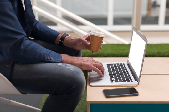 Businessman having coffee while using laptop