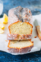 Sliced lemon poppy seed pound cake covered with a glaze on a wire rack. Blue stone background. Close up