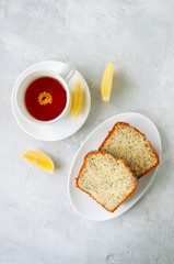 Fototapeta na wymiar Lemon poppy seed cake and a cup of tea on a white stone background.