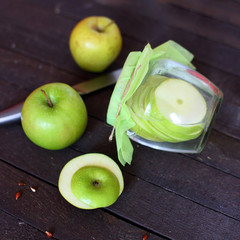water with green Apple in jar on wooden background