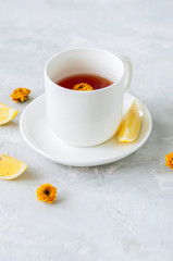 Obraz na płótnie Canvas One cup of flower tea, lemon slices and dried flowers on a white stone background.