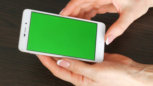 Female hands with beautiful French manicure take a white smartphone with Green Screen. Using Smartphone,Holding Smartphone with Green Screen