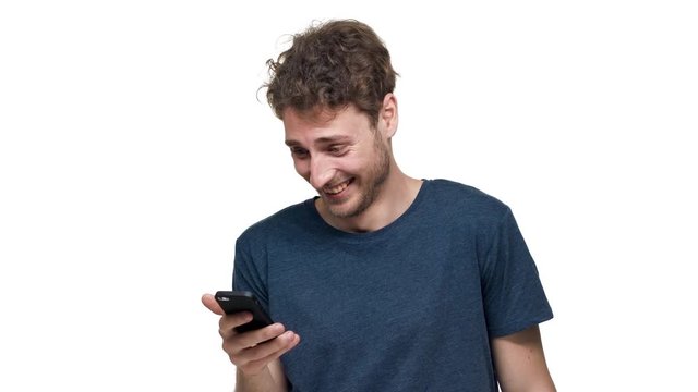 Portrait of content attractive man using mobile phone and laughing in happy mood, isolated over white background in studio closeup. Concept of emotions