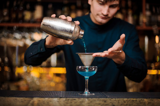 barman in a blue shirt filters an alcohol cocktail Blue Lagoon