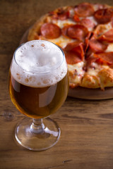 Beer and pepperoni pizza on wooden table. Glass of beer. Ale and food concept. vertical