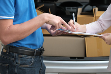 Obraz premium woman signing signature on clipboard to receive package from delivery man. male postal courier person deliver box