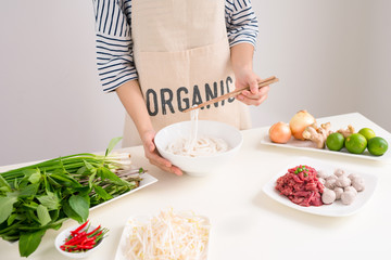 Female chef prepare traditional Vietnamese soup Pho bo with herbs, meat, rice noodles