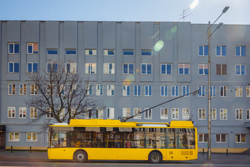 A yellow trolleybus is standing at a bus stop near the big house