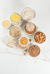 Selection various types cereal grains groats  in different bowl on white marble background, copy space above