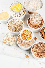 Selection various types cereal grains groats  in different bowl on white marble background, copy space top view