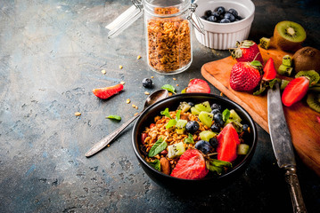 Healthy breakfast with muesli or granola with nuts and fresh berries and fruits - strawberry, blueberry, kiwi, on dark blue table, copy space