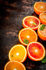 Fresh raw blood oranges, halves, with mint, on dark rusty background copy space