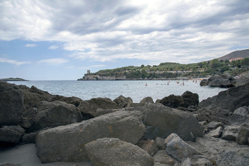 Fototapeta na wymiar People enjoying in a bay with big stones on the sandy beach