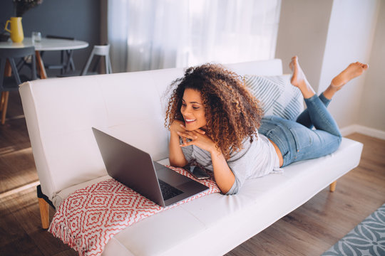 african happy woman lying on couch with laptop