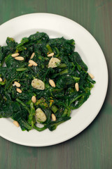 greens with garlic on white plate on wooden background