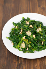 greens with garlic on white plate on wooden background