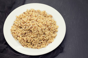 boiled quinoa on white plate on black ceramic background