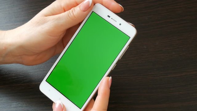 Female hands with beautiful French manicure take a white smartphone with Green Screen. Using Smartphone,Holding Smartphone with Green Screen