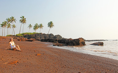Beach with black sand and palm trees. Dark brown volcanic sand and beach in India, GOA