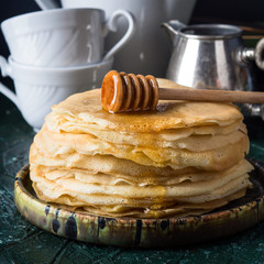Stack of crepes with poured honey on dark background