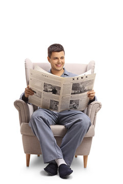 Young guy in pajamas sitting in an armchair and reading a newspaper