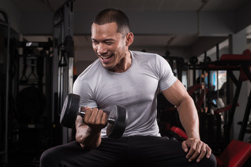 Muscular builder man training his body with dumbbell in Modern fitness center