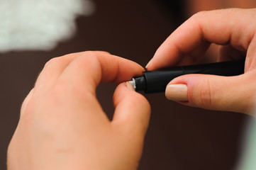 Woman taking blood sample with lancet pen on wooden background. Diabetes concept.