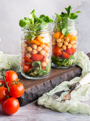 Fresh salad lunch with chickpeas, tomatoes, carrots and valerian served in mason jars