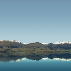 Fototapeta na wymiar Landscape of snowy mountain peaks with blue and clear sky in front of a huge calm lake. The mountains are reflected on the water like a mirror.