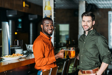 handsome happy men with mugs of beer at bar counter looking at camera