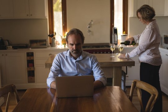 Man working on laptop while woman pouring champagne into glass