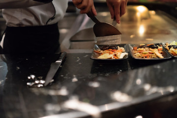 Hand of Chef cooking salad on hot pan in front of customers.