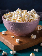Popcorn in pink bowl on wooden board on dark green background