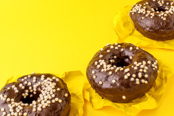 composition of three chocolate donuts, on a yellow background
