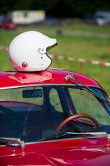 red classic car waiting at the pit for the great race with white helmet resting on the car roof