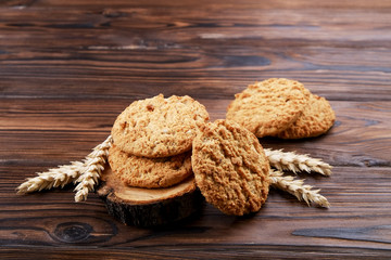 Healthy vegan integral cookies made of hazelnut powder on wooden slice coaster, wood table background. Home made vegetarian, gluten free snack with nuts. Decorative wheat spica. Close up, copy space.