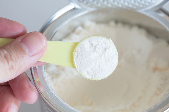 hand holding milk powder in measuring spoon for baby.