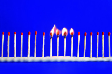 Line of red unused and four burning safety matches on bright blue background with copy space for text. Concept of teamwork, work together one after another and follow leaders.